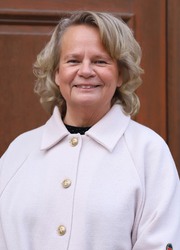 Jonna Lindman, kommunstyrelsens ordförande, som står framför en ekdörr. Hon är klädd i en vit kappa med guldfärgade knappar.